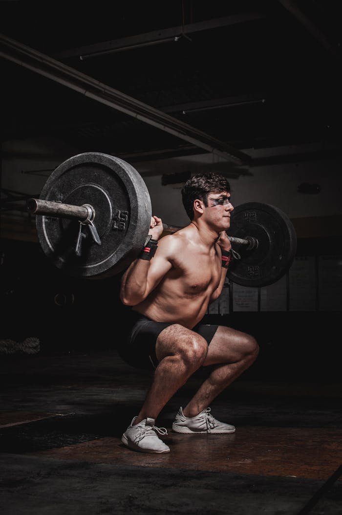 about-01 Shirtless man performing a barbell squat, showcasing strength and fitness.